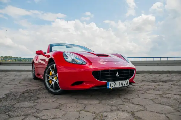 Czerwone Ferrari California z żółtymi zaciskami hamulcowymi na tle błękitnego nieba z chmurami.