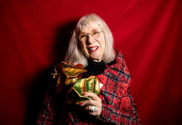 Suzanne på scen, glad och med ett glittrande pris i famnen, klädd i en röd rutig kavaj mot en röd bakgrund.