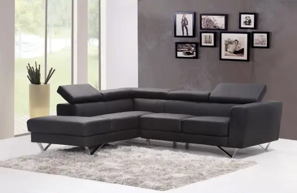 Divano angolare in pelle grigio antracite scuro, con tappeto soffice e cornici decorative alle pareti.