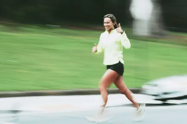 Donna sorridente corre con pollice in su, indicando un ottimo ritmo medio corsa.