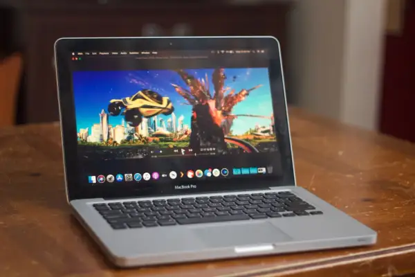 A MacBook Pro displays the "Speed Racer" trailer on the IINA player, showing a futuristic city and a car mid-explosion.