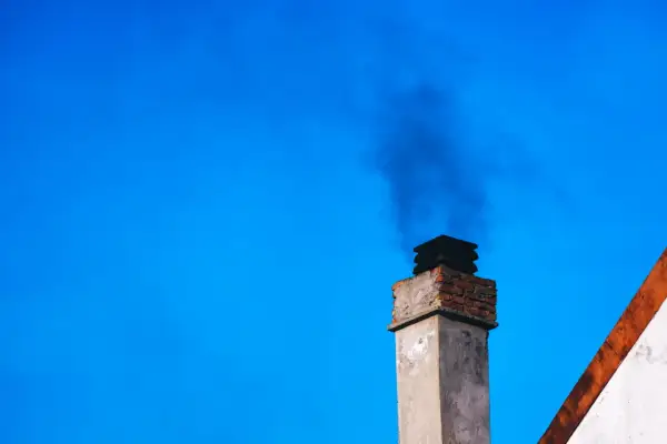 Dym z komina, być może dzięki zastosowaniu filtra kominowego zamiast wymiany pieca, unosi się na tle błękitnego nieba.