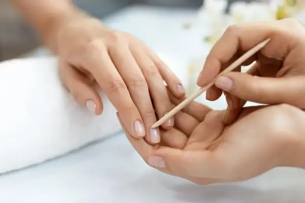 Delikatne dłonie poddawane zabiegowi manicure biologicznego. Paznokcie są naturalne, zadbane, a skórki delikatnie odsuwane patyczkiem.