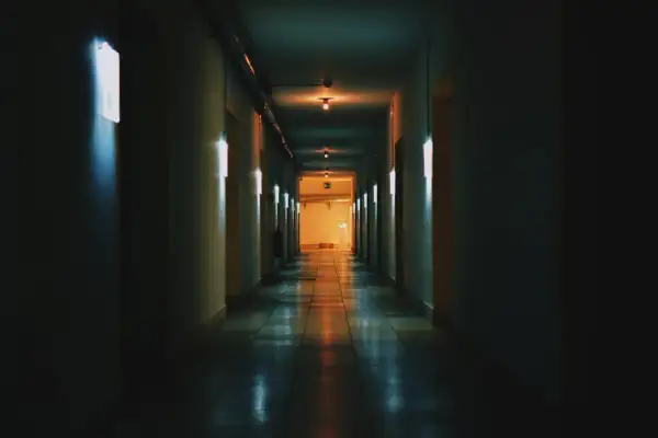 Un corridoio buio con luci al neon che cercano di rendere luminoso lo spazio. La prospettiva crea un senso di profondità.