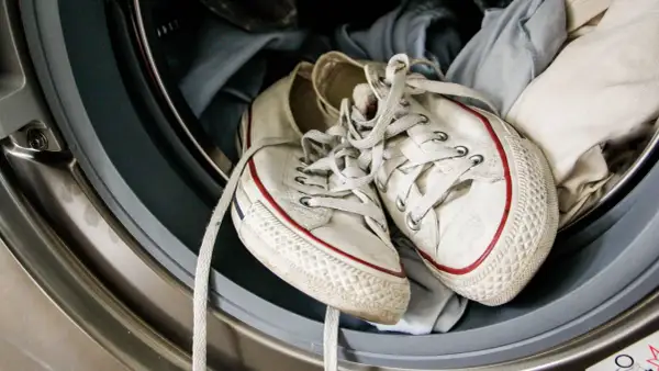 Weiße Turnschuhe mit roten Streifen liegen in der Waschmaschine, bereit zum Laufschuhe waschen.
