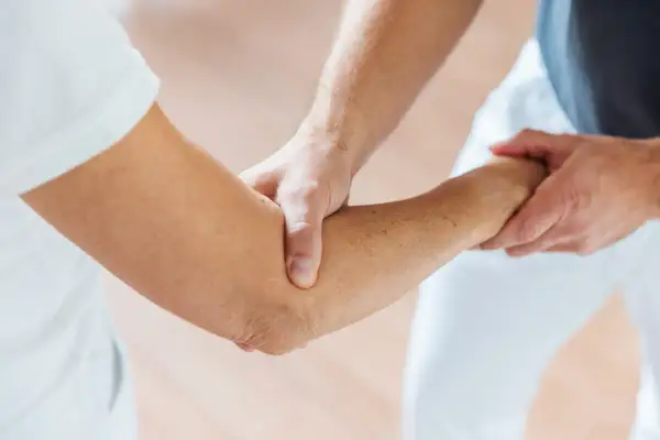 Physiotherapeut hilft beim Ellenbogen mobilisieren nach OP. Sanfte Berührung zur Wiederherstellung der Beweglichkeit.