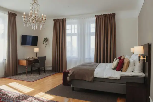 Ett elegant hotellrum på hotel Drott Karlstad med en stor säng, skrivbord och kristallkrona.