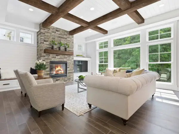 Cozy living room with a stone fireplace, tufted sofa, and an accent ceiling with exposed wooden beams.