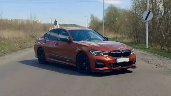 Pomarańczowe BMW 330i G20 na drodze, z widocznymi czarnymi felgami i detalami aerodynamicznymi.
