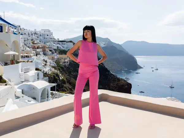 Modelka w różowym komplecie, idealna odpowiedź na pytanie: jaka bluzka do różowych spodni? Tło to malownicza Santorini.