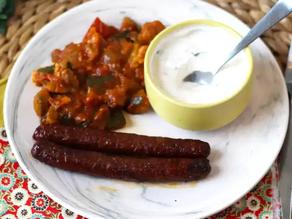 Dos salchichas merguez que es picantes, acompañadas de un guiso de verduras y una salsa cremosa.