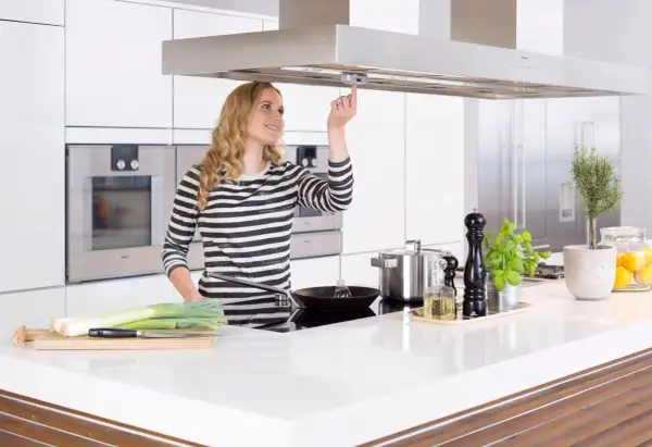 Junge Frau bedient Dunstabzugshaube mit Herd-Abschaltautomatik. Sicheres Kochen für Senioren.