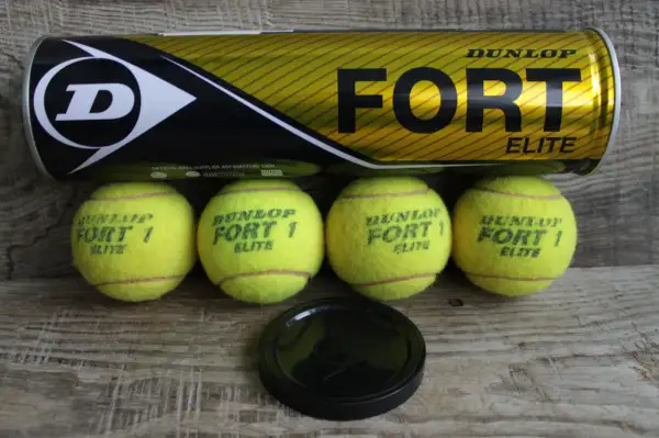 Lattina Dunlop Fort Elite e quattro palline da tennis gialle su fondo in legno. Pronte per una partita!