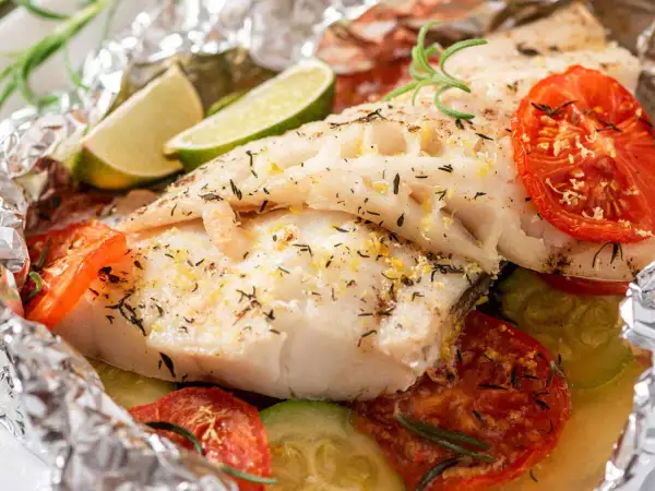 Poisson en papillote savoureux, avec tomates, courgettes, citron vert et romarin, le tout emballé dans du papier aluminium.