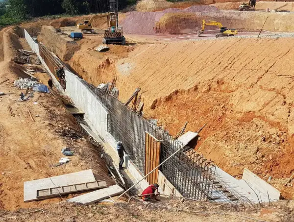 Budowa muru oporowego, gdzie pracownicy przygotowują zbrojenie. Widać koparki i wykop. To kluczowy etap, by wiedzieć, ile potrzeba betonu na fundamenty.