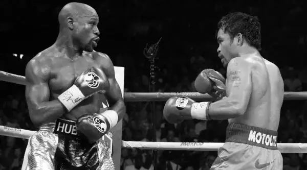 Floyd Mayweather Jr. in his signature defensive stance, facing Manny Pacquiao in a boxing ring.