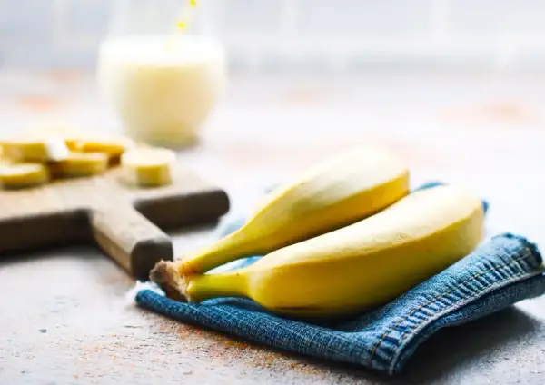 Dwa dojrzałe banany na dżinsowej serwetce, obok pokrojonych bananów i szklanki napoju. Interesuje Cię indeks glikemiczny bananów?