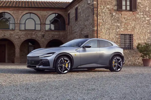 Srebrny Ferrari SUV Purosangue zaparkowany przed kamiennym budynkiem z łukowymi oknami.