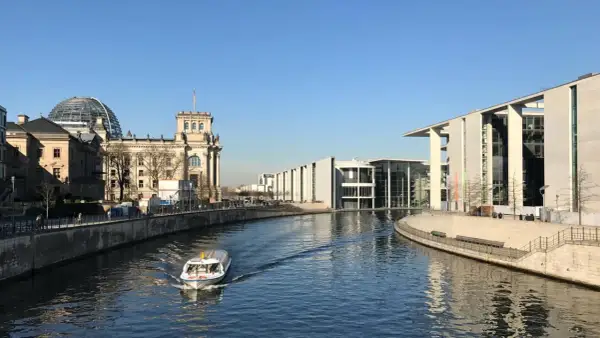 Ein Boot fährt auf der Spree am Reichstagsgebäude und modernen Gebäuden des Regierungsviertels Berlin vorbei.