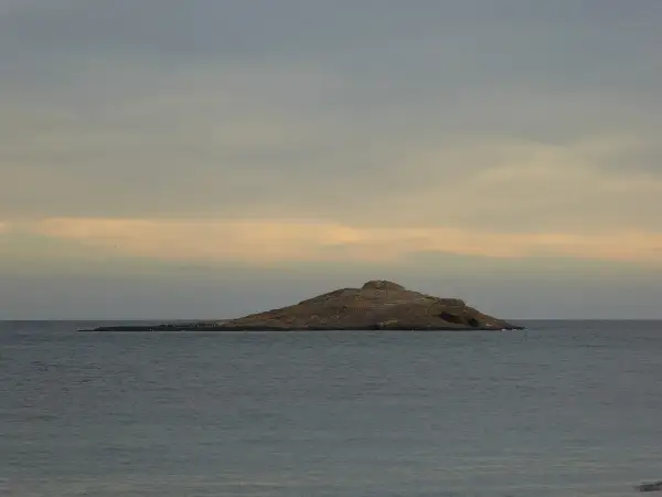 Isla de San Andrés, Almería, un islote rocoso en el mar con gaviotas posadas. Cielo nublado con tonos anaranjados.