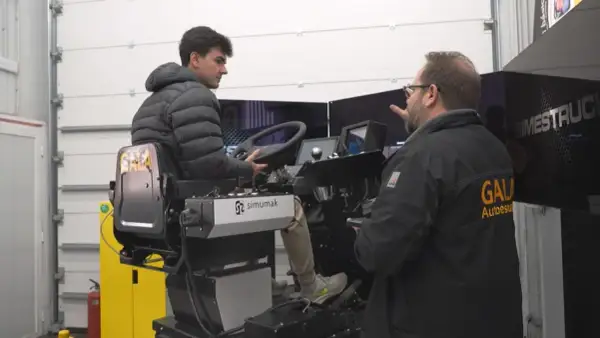 Profesor de autoescuela instruye a un alumno en un simulador de camión. El alumno practica al volante mientras el profesor le da indicaciones.