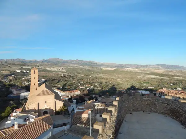Vistas de Serón que ver: iglesia con campanario, tejados y paisaje rural montañoso bajo un cielo azul.
