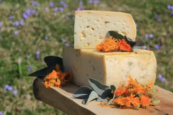 Due blocchi di formaggi di montagna, uno sopra l'altro, decorati con fiori arancioni e foglie verdi su un tagliere di legno.