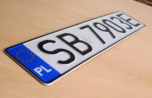 Nowe tablice rejestracyjne z oznaczeniem PL i numerem SB 79035 leżą na drewnianym blacie.