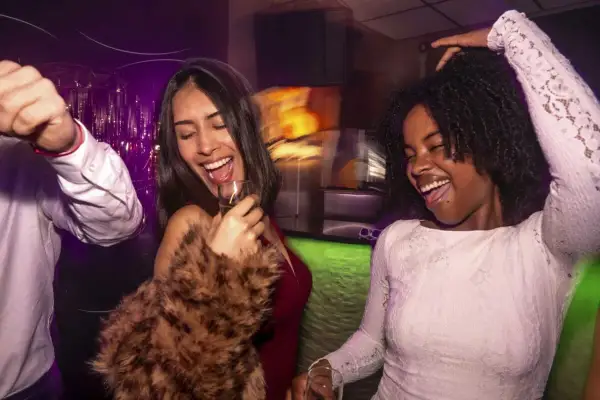 Zwei Frauen tanzen ausgelassen auf einer flinta party hamburg. Sie lachen und halten Gläser in der Hand.
