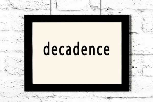 Czarno-biały obraz z napisem "decadence" na jasnym tle, wiszący na białej ceglanej ścianie. To pytanie: co to dekadentyzm?