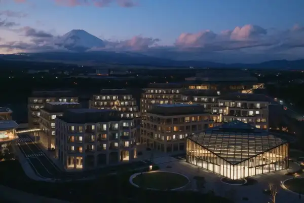 Nowoczesne budynki z oświetlonymi oknami i górą Fudżi w tle o zmierzchu.
