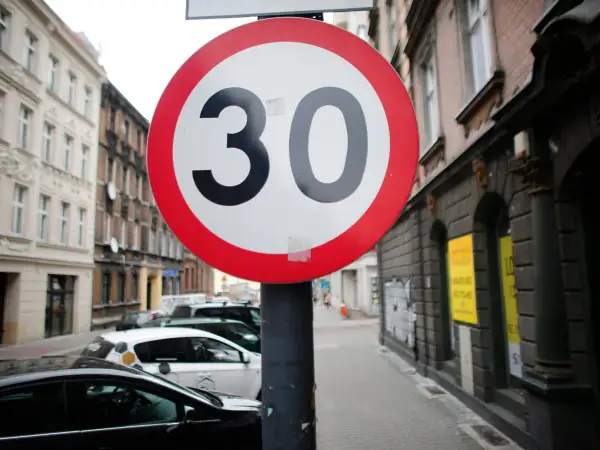Znak ograniczenia prędkości do 30 km/h. Czy skrzyżowanie odwołuje ograniczenie prędkości? Ulica z samochodami i kamienicami.