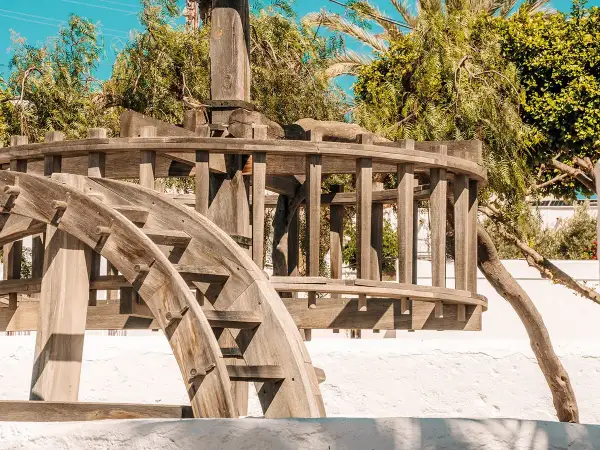 El pozo de los frailes que ver: una noria de madera antigua, rodeada de vegetación exuberante y bajo un cielo azul brillante.