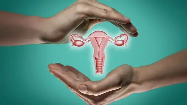 Dłonie otaczają macicę z jajowodami. Ilustracja symbolizuje troskę o zdrowie reprodukcyjne i zamkniętą szyjkę macicy - jak wyczuć jej stan.
