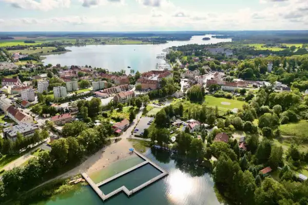 Widok na Ryn z lotu ptaka. Widać jezioro, miasto, plażę i basen. To świetne miejsce na wakacje, pełne atrakcji dla dzieci.