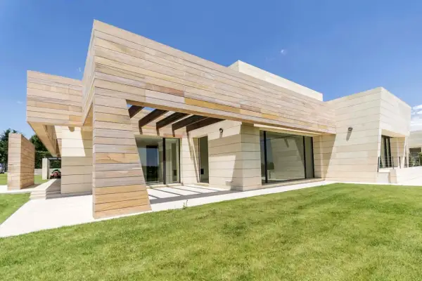 Moderna finca en Madrid con fachada de piedra y madera, césped verde y cielo azul.