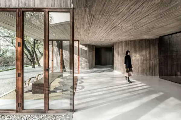 Interior moderno con paredes y techos de hormigón texturizado. Una mujer camina por los suelos de hormigón pulido, proyectando sombras.