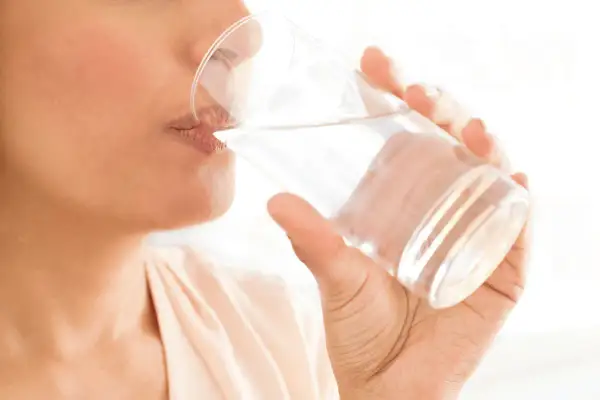 Une personne boit un verre d'eau, un geste simple pour savoir comment bien s'hydrater et rester en forme.