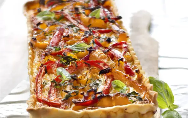 Tarte rectangulaire aux poivrons rouges et jaunes grillés, garnie de basilic frais. Un délice coloré et savoureux.