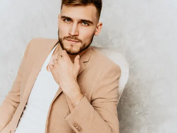 Elegancki mężczyzna w beżowej marynarce, zamyślony, być może zastanawia się, czego pragną mężczyźni.