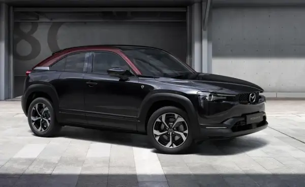 Czarna Mazda MX-30 z czerwonym dachem, prezentująca swoje kompaktowe mazda mx 30 wymiary, stoi przed betonową ścianą z numerem 80.