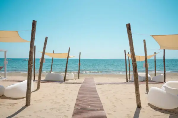 Un percorso in legno conduce al mare cristallino del golfo di Follonica, tra comode sedute bianche e tende parasole.