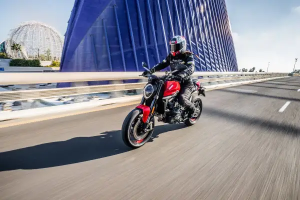 Mujer conduce moto roja por puente moderno. Con 18 años, puedes sacarte el carnet de moto A2.