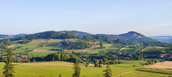 Zielone wzgórza i pola tworzą malowniczy krajobraz, przypominający krainę wygasłych wulkanów. W oddali widać lasy i niewielkie osady.