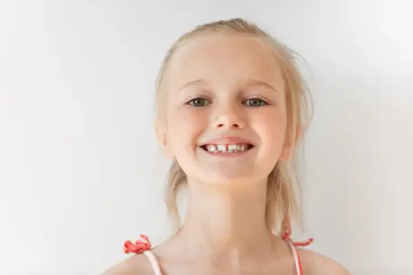 Uśmiechnięta dziewczynka z blond włosami, kiedy rosna 6 ząbków, pokazuje swoje nowe mleczaki.
