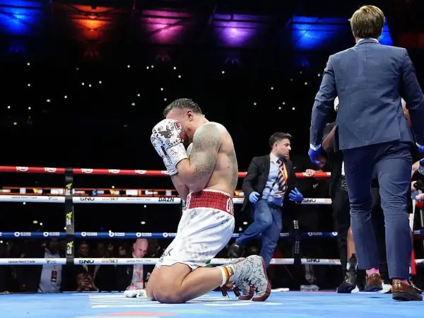 A boxer kneels in the ring, head in hands, after a tough fight. The Dubois vs Usyk bout ends with a somber moment.