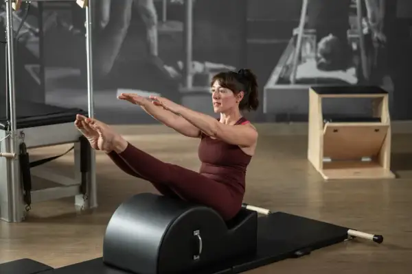 Donna in posa di equilibrio sul reformer Pilates, con le gambe sollevate e le braccia tese. Il suo sguardo concentrato esprime il **core significato** di forza e controllo.