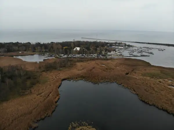 Widok na port jachtowy i jezioro otoczone trzcinami. W oddali widać morze i falochron. To malownicze **górki zachodnie**.