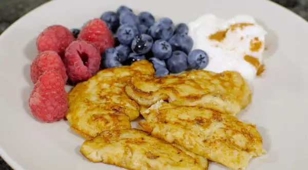 En tallrik med gyllene pannkakor, färska hallon, blåbär och en klick yoghurt med kanel. Perfekt för diabetes mat recept.