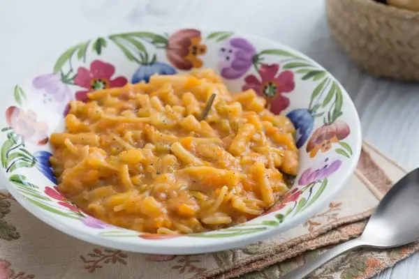 Un plat réconfortant de pâtes italiennes avec de la pomme de terre et des légumes, servi dans un bol fleuri.